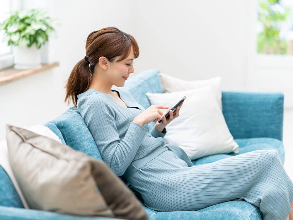 ソファーに座ってスマートフォンを操作している女性