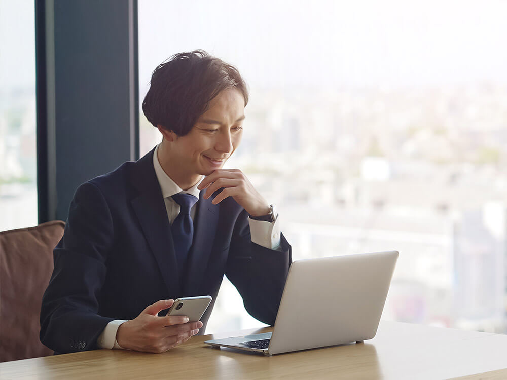 スマホとPCを操作しているスーツ姿の男性