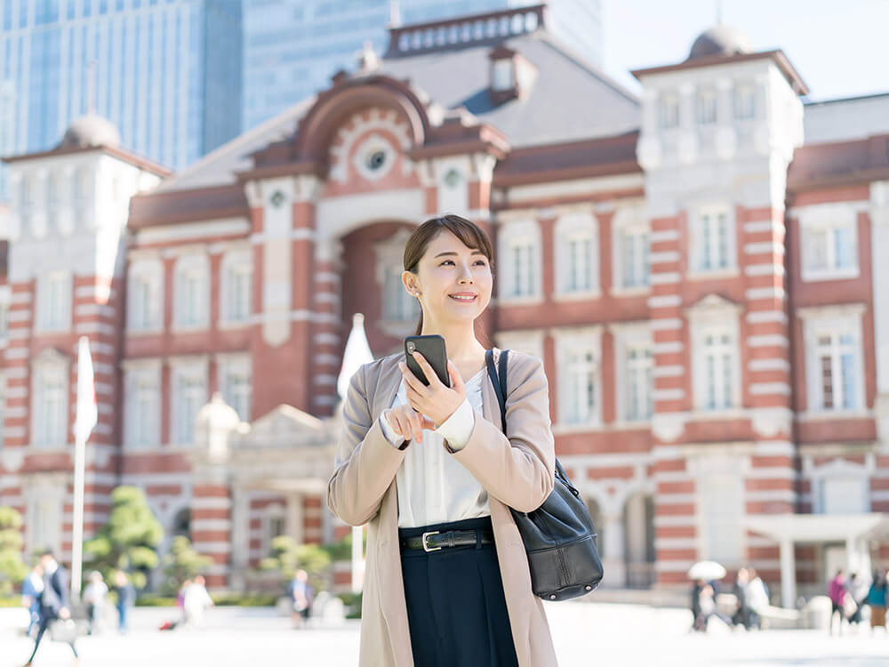 駅の前でスマートフォンを見ている女性