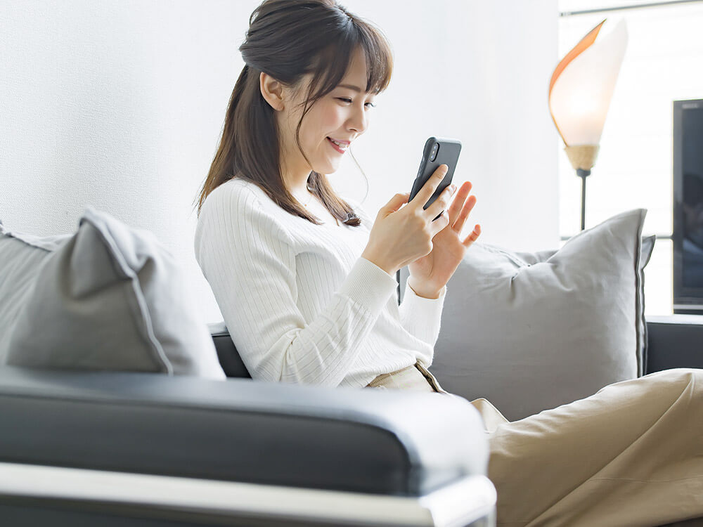 ソファーに座ってスマートフォンを操作している女性